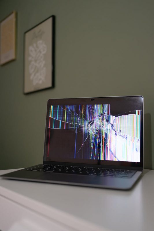 pexels-photo-28379995 A laptop with a cracked and malfunctioning screen displayed on a desk indoors.